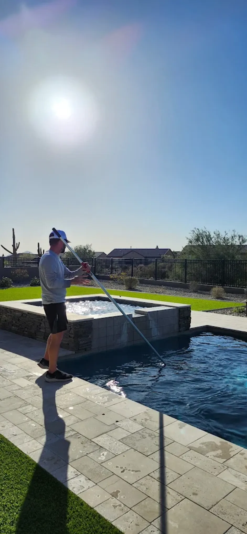 A Sapphire Pools technician brushing a residential pool beside a spillover spa in Fountain Hills, Arizona